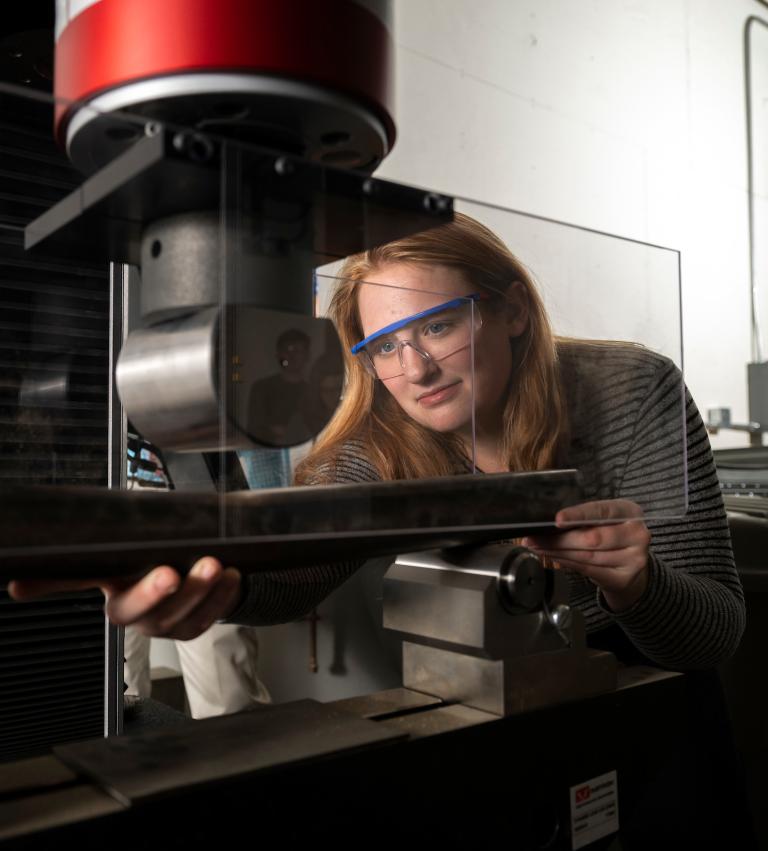 A student wears safety goggles as she adjusts machinery in the engineering lab.