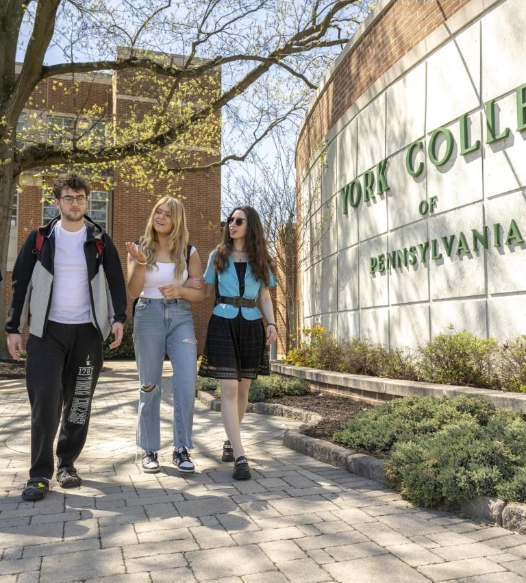 Students walk in front of the York College sign on spring day