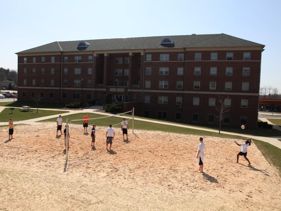 Students playing a beach volleyball game in front of a residence call
