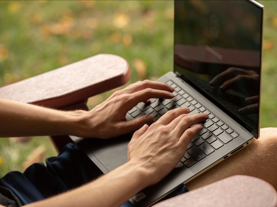 A close-up of a laptop on the lap of someone sitting outdoors.