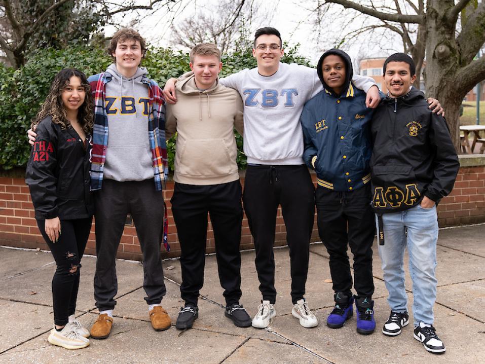 Six students dressed in Greek Life swag pose for a group photo on campus.