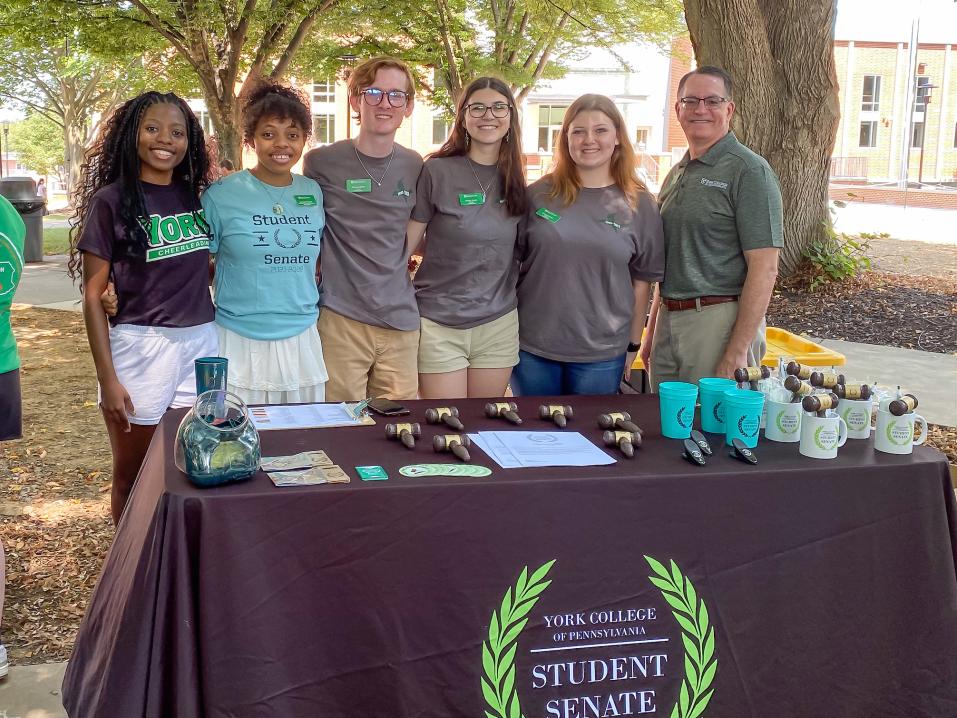 A group of five student senators pose by their involvement fair table with President Thomas Burns.