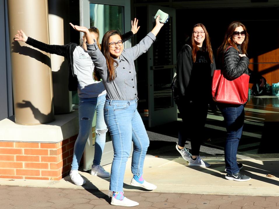 A student throws her arms up in the air and smiles while walking into the Waldner Performing Arts Center