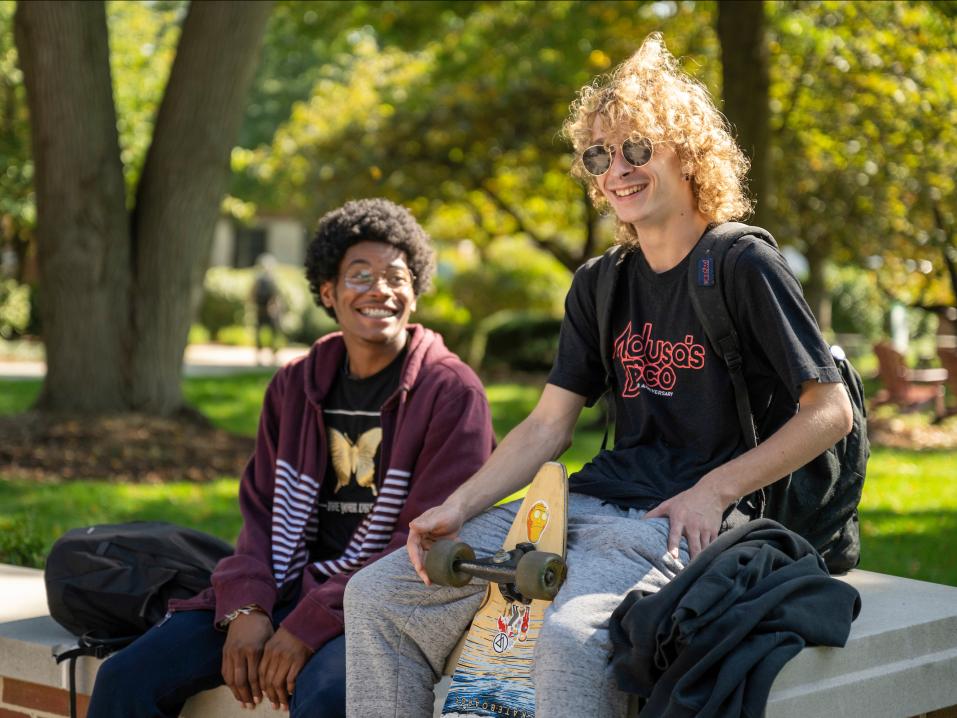 two students sitting and laughing outside on campus.
