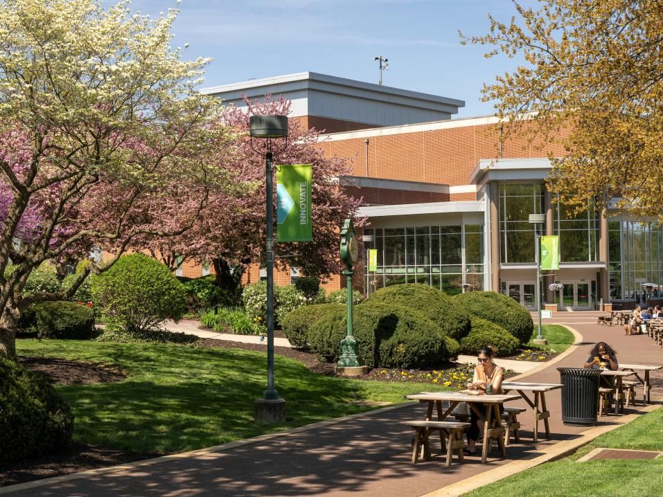 An image of main campus in the spring. Students are sitting at table studying outside of the WPAC building.