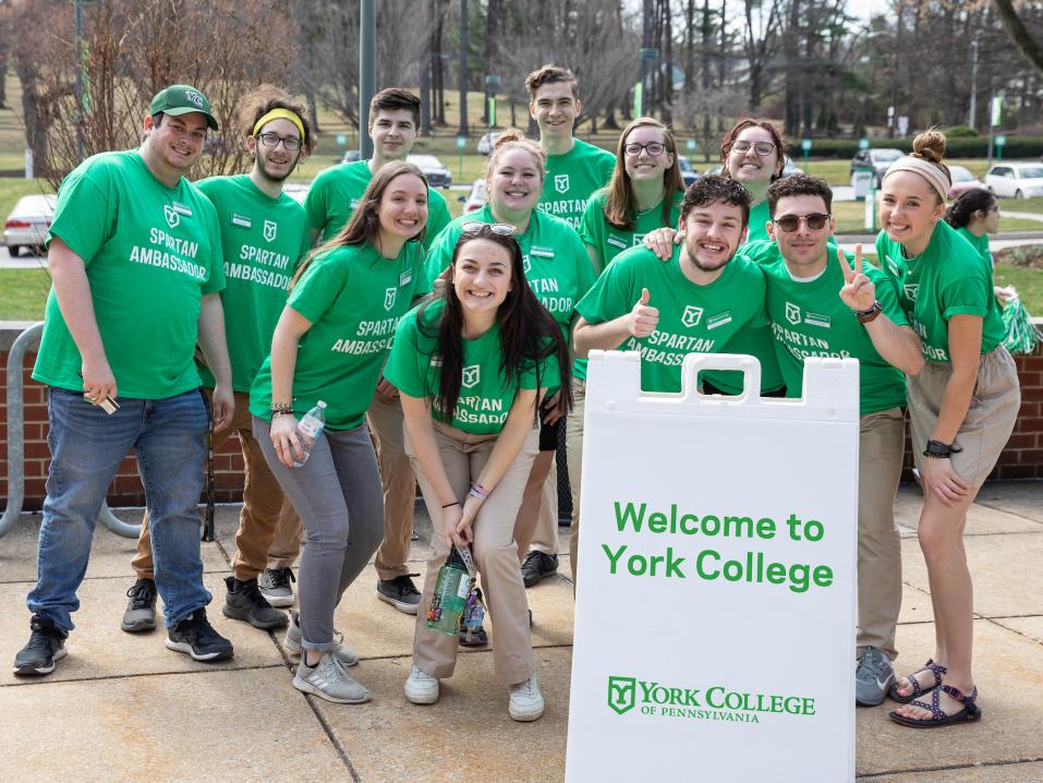 Group of students wearing green shirts in front of a "welcome to York College" sign