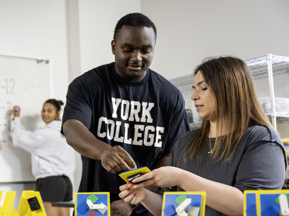 Two students work on a clock while a third student writes on the board behind them.