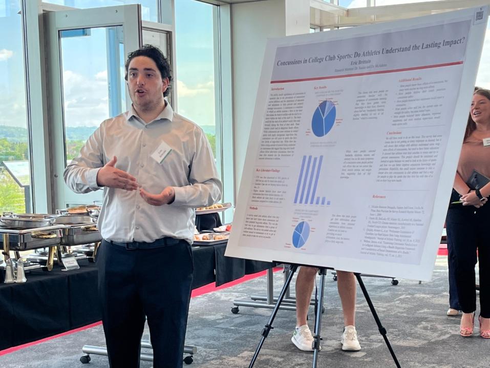 Man presenting a poster on concussions in college club sports at an indoor event.