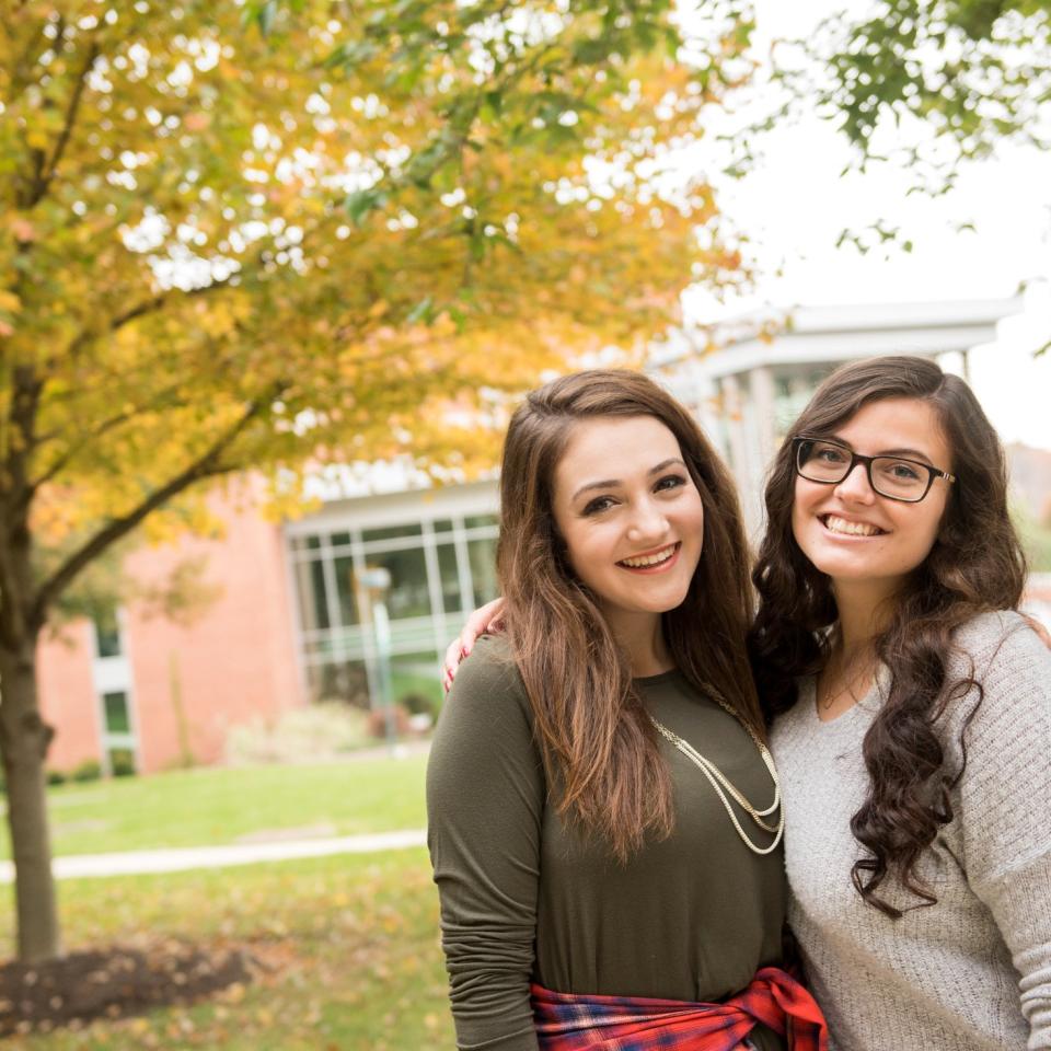 Two students pose together on campus pathway with trees in background