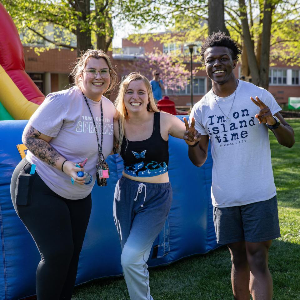 Three students smile and pose in front of an inflatable slide.