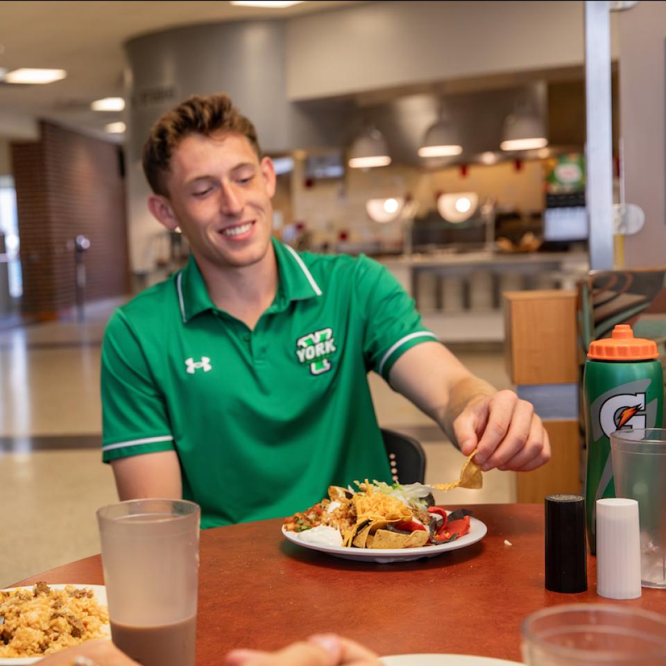 A student smiles as he eats in the seating area of West Campus DIning Hall.