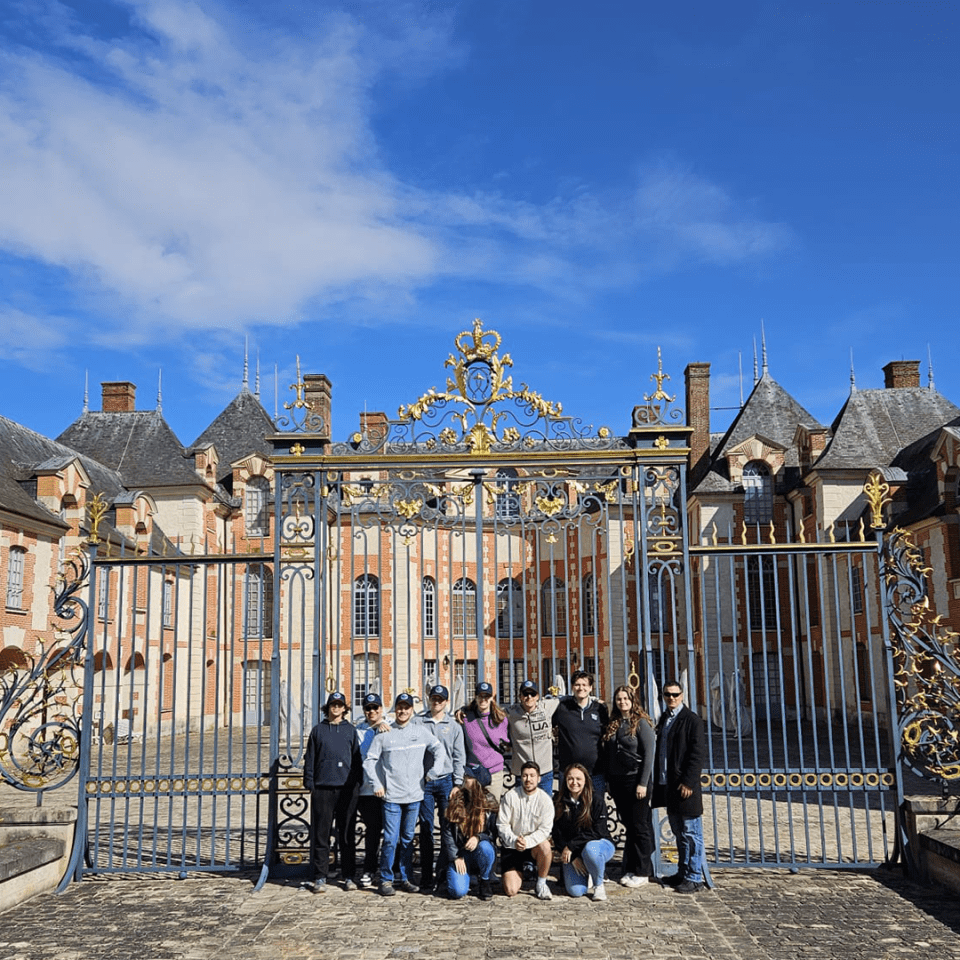 A group from the International Sport and Entertainment course pose in front of an ornate gate with a European building behind it.