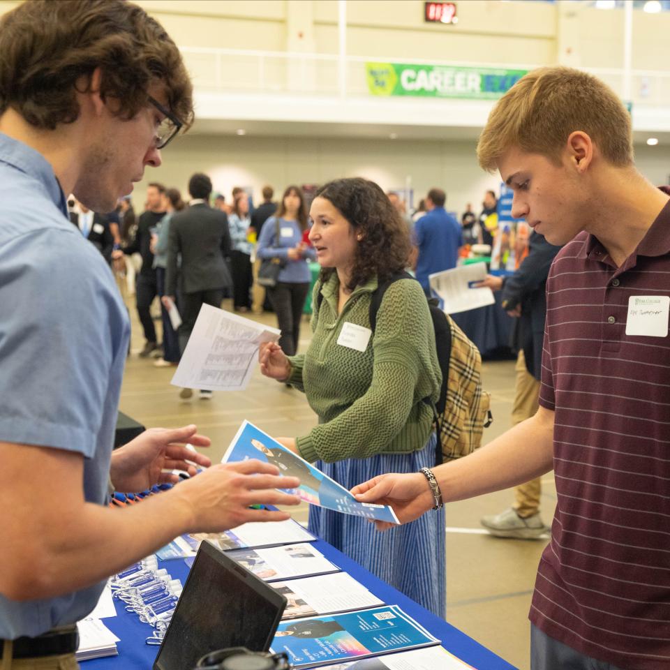 A student at a career expo takes a flyer from an employer representative.