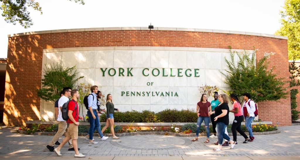 Two groups of students converge together in front of York entrance sign