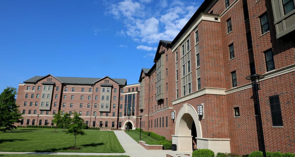 Five-story, red brick residence halls surrounded by green space and trees.