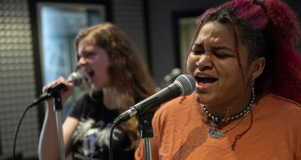 Two students sing into microphones in the music recording studio.
