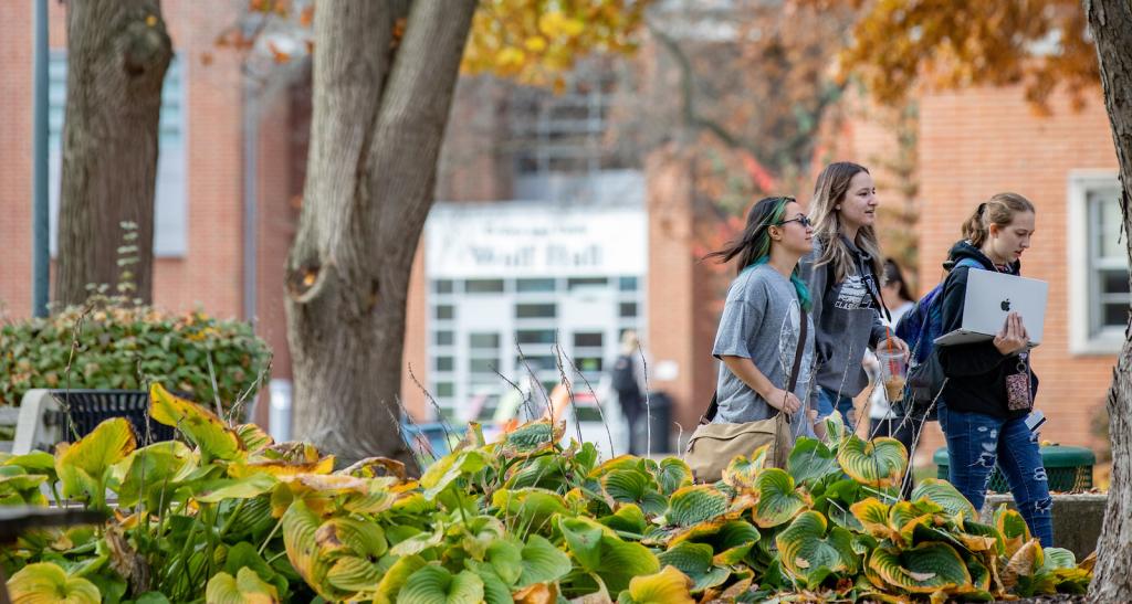 Three students walk across campus on a fall day.