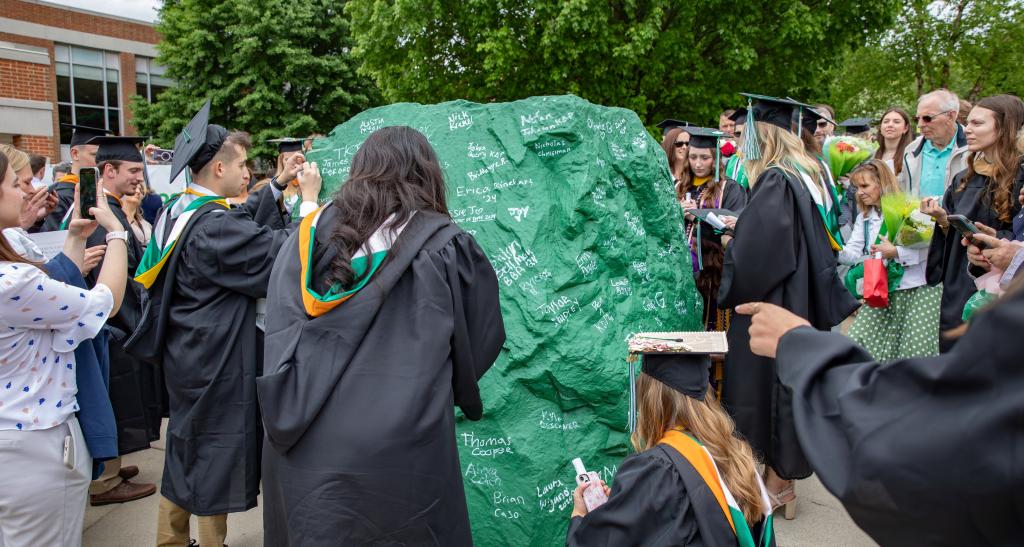 Graduates gather around the Rock on Commencement day to signify the completion of their academic journey. The Rock is painted York College green and the graduates' markers are filled with white ink.