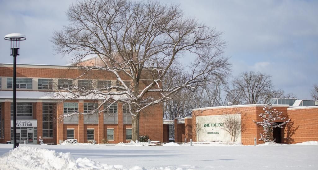 Campbell Hall and a large wall with the York College of Pennsylvania wordmark are visible in a field of snow.