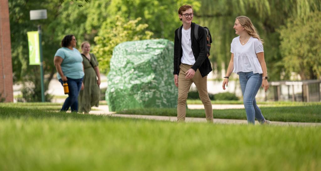 Two students walking on campus near the campus rock