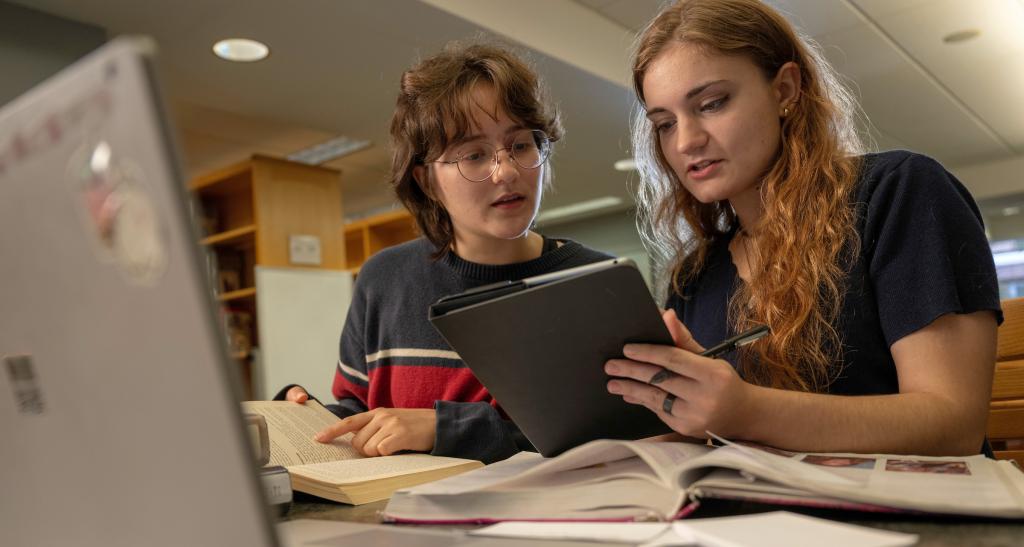 Two students looking at a tablet while studying in the library.