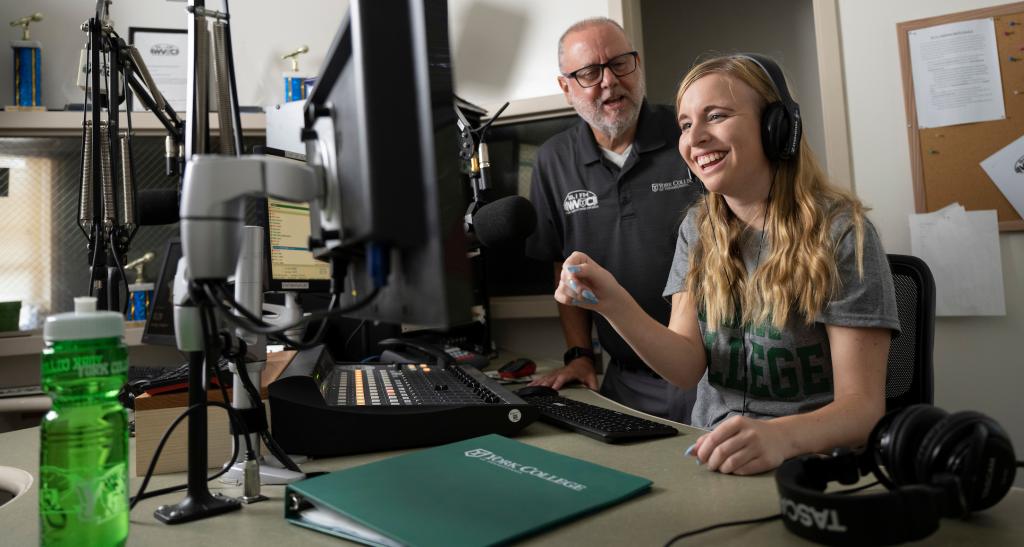 A student with a professor in the radio station on campus.
