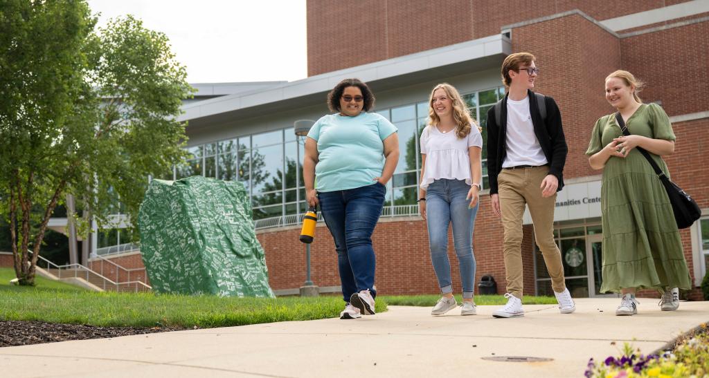 Four students walking and talking near The Rock on campus.