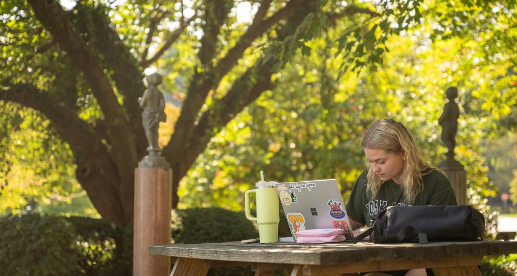 Student sitting at table outside with their laptop studying