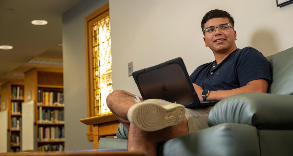 A student sitting with his laptop in the library.