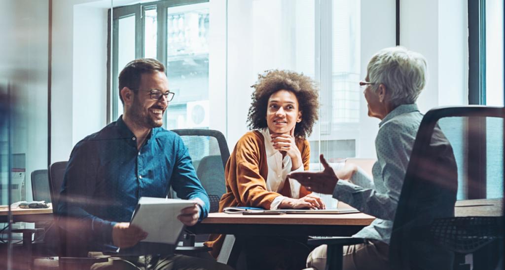 Three professionals meet in a glass-walled conference room, gathered around a table.