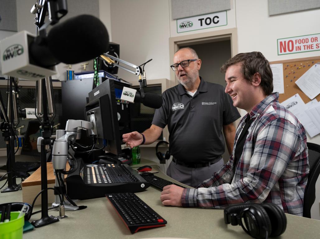 A student with a professor in the broadcasting studio learning how to use equipment.