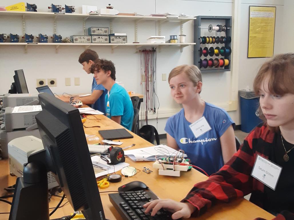 Four high school students sit at computers along a desk in the Engineering Center.