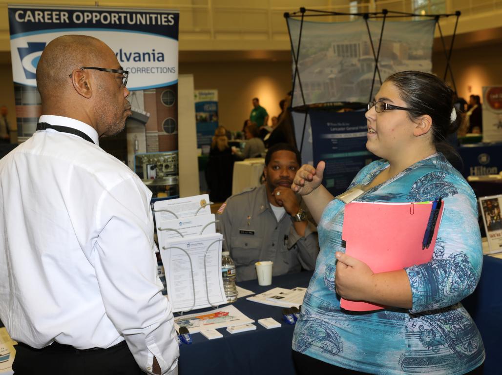 A student holding a pink binder gestures as she speaks to a business representative at the Career Expo at York College.