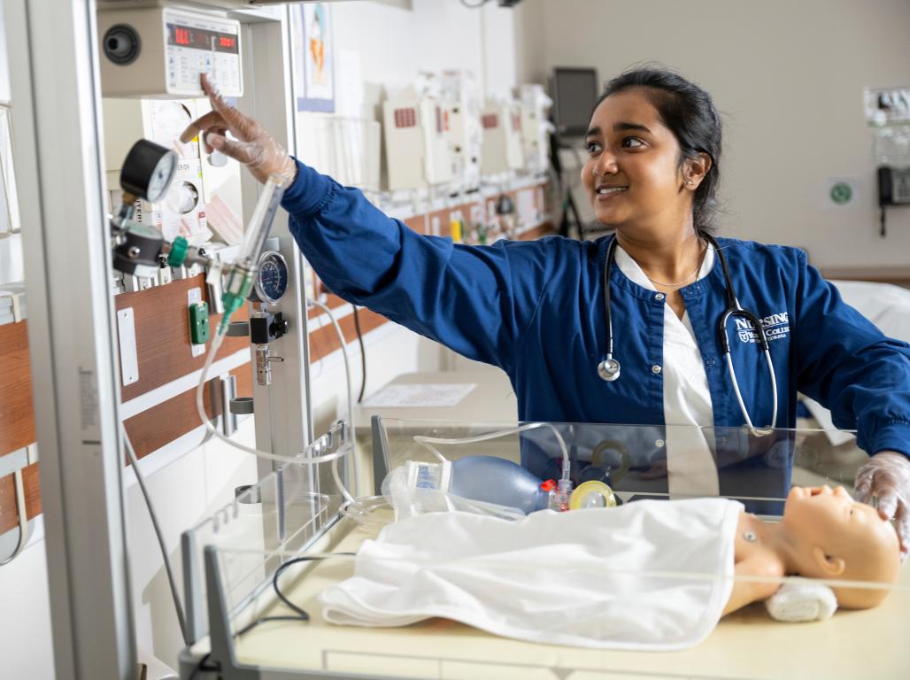 Khushi Iyer, wearing a nursing scrubs uniform, reaches for equipment in the nursing simulation lab.