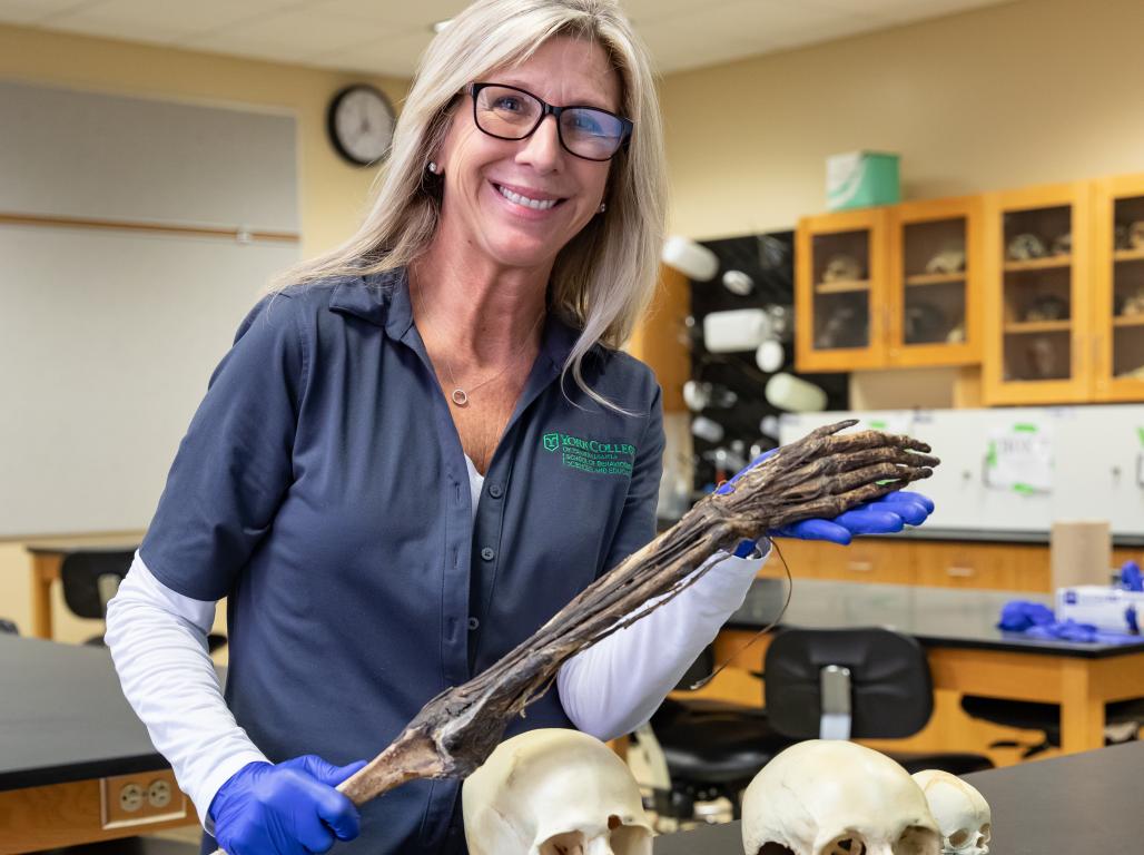 Barb Hanbury poses in the lab next to two skulls on the exam table.