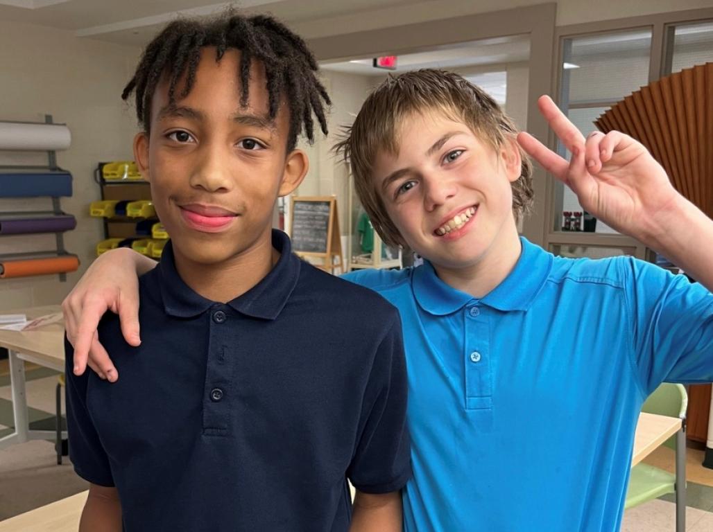 Two boys pose for the camera. One had his arm over shoulders of the other and make a peace gesture with his other hand.