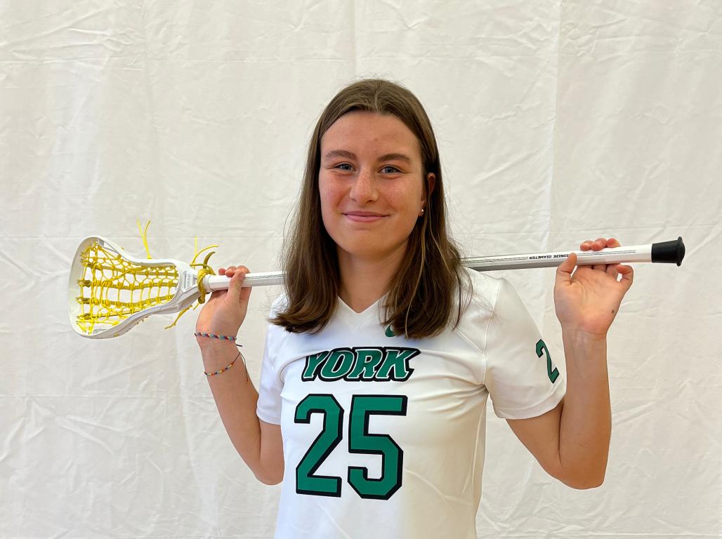 Katie Jeanes poses for a photo in her lacrosse uniform, holding a lacrosse stick across her shoulders.