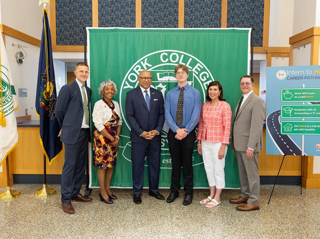 Dr. Josh DeSantis, Rep. Carol Hill-Evans, PA Auditor General Timothy L. DeFoor, student Cade Ham, Rep. Kristin Phillips-Hill, and YCP President Thomas Burns pose for a group photo in front of the press conference stage.