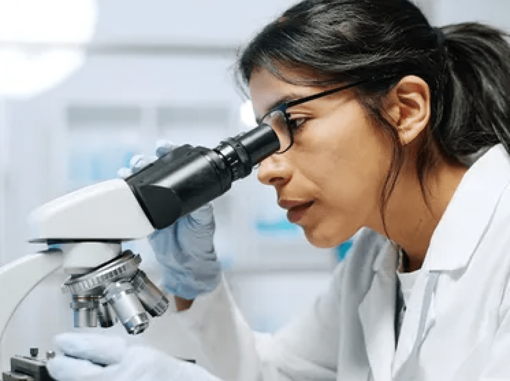 A scientist looks into a microscope in a lab.