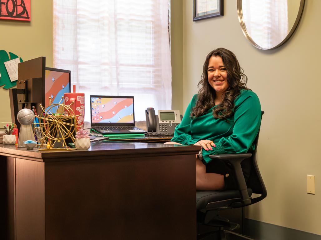 Mady Sharp sitting at her desk, smiling.