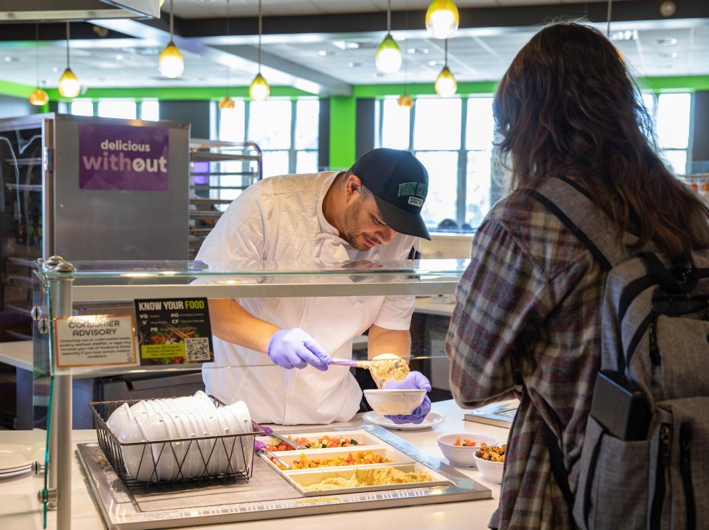 Chef Hector plates food for a student in line at the dining hall.