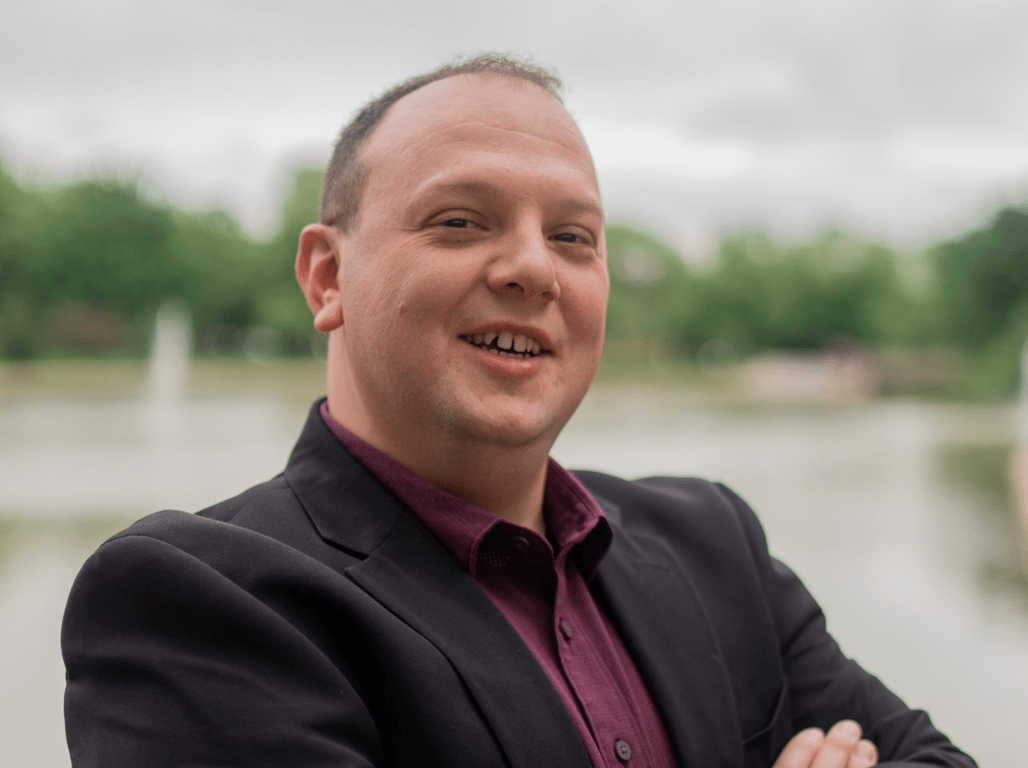 Bryan Sheaffer poses for a photo as he wears a suit and stands by a river.