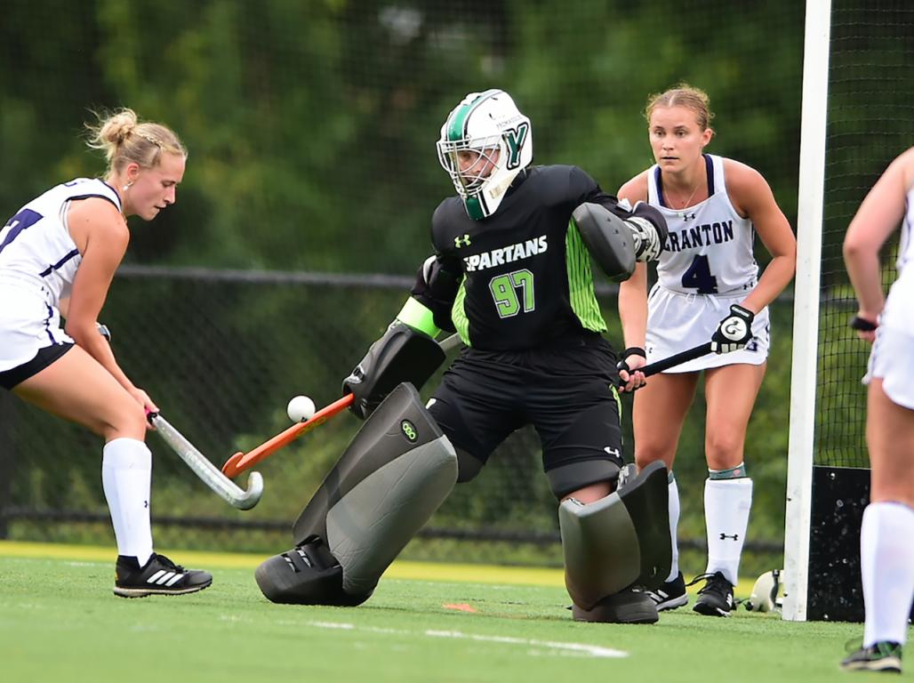 York College field hockey goalie, Belle Fields, makes a save while being surrounded by several players from the opposing team.