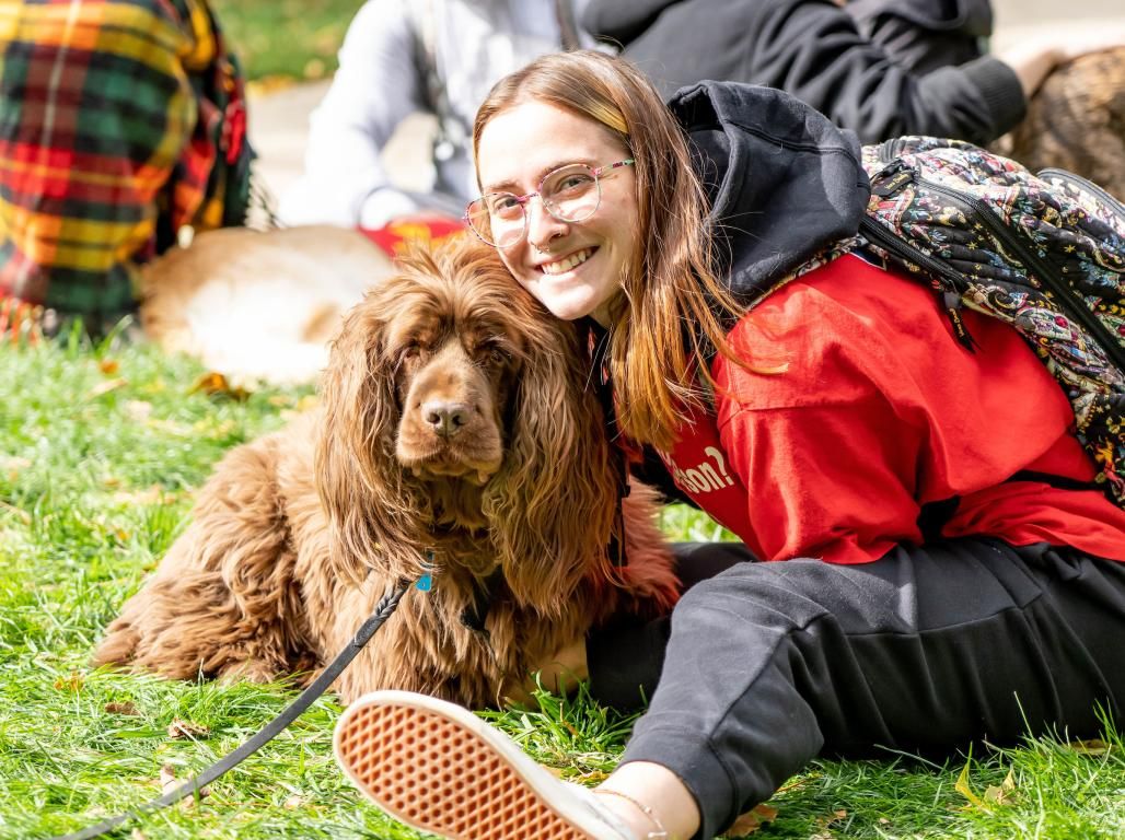 A student smiles as she snuggles with a therapy dog on the campus lawn.