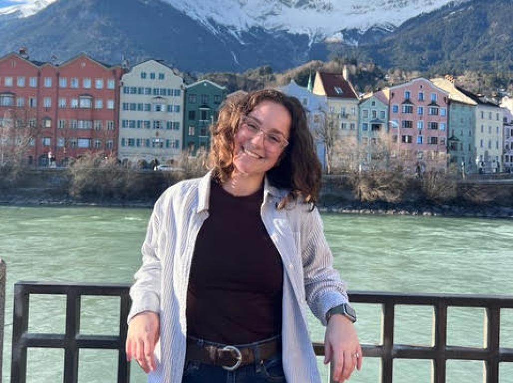 Gia Levis smiling in front of a scenic view of Innsbruck, Austria's mountains, houses, and a river.