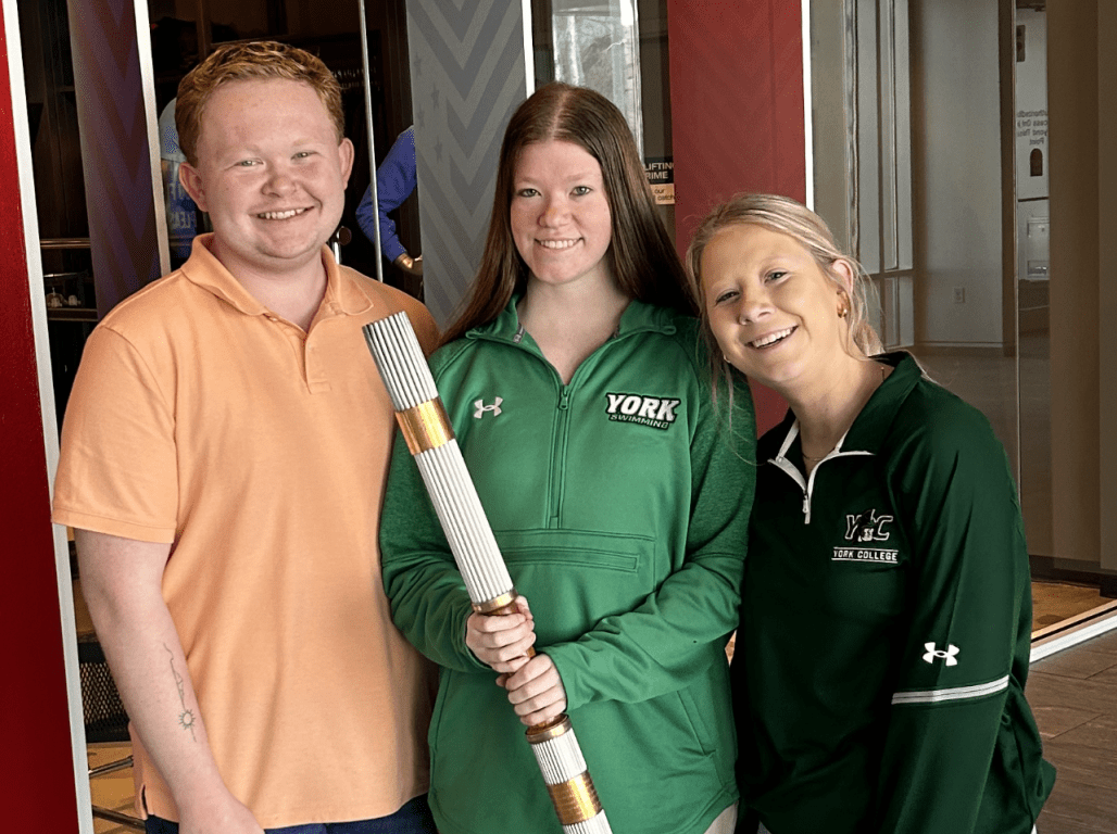 Three York College students smile as they hold the Olympic torch from 1996.