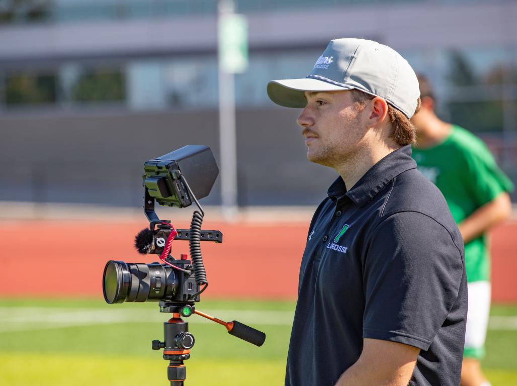 AJ Apel standing on the athletic field with his camera on a tripod.