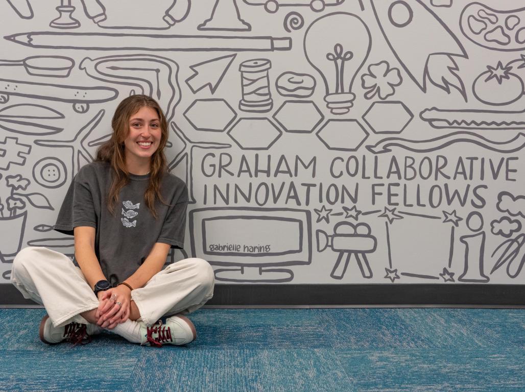 Alumna Gabrielle Haring sits in front of a Mural painted for the GCCI