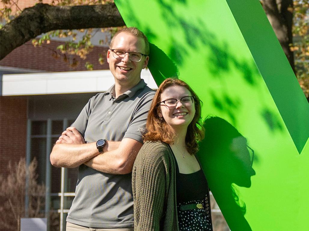 Aaron Owens and another student stand next to the letter Y statue near the Student Union building