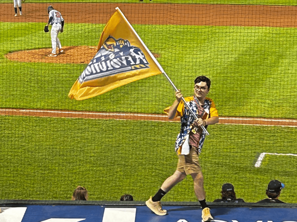 Person walking across a baseball field waving a large yellow flag.